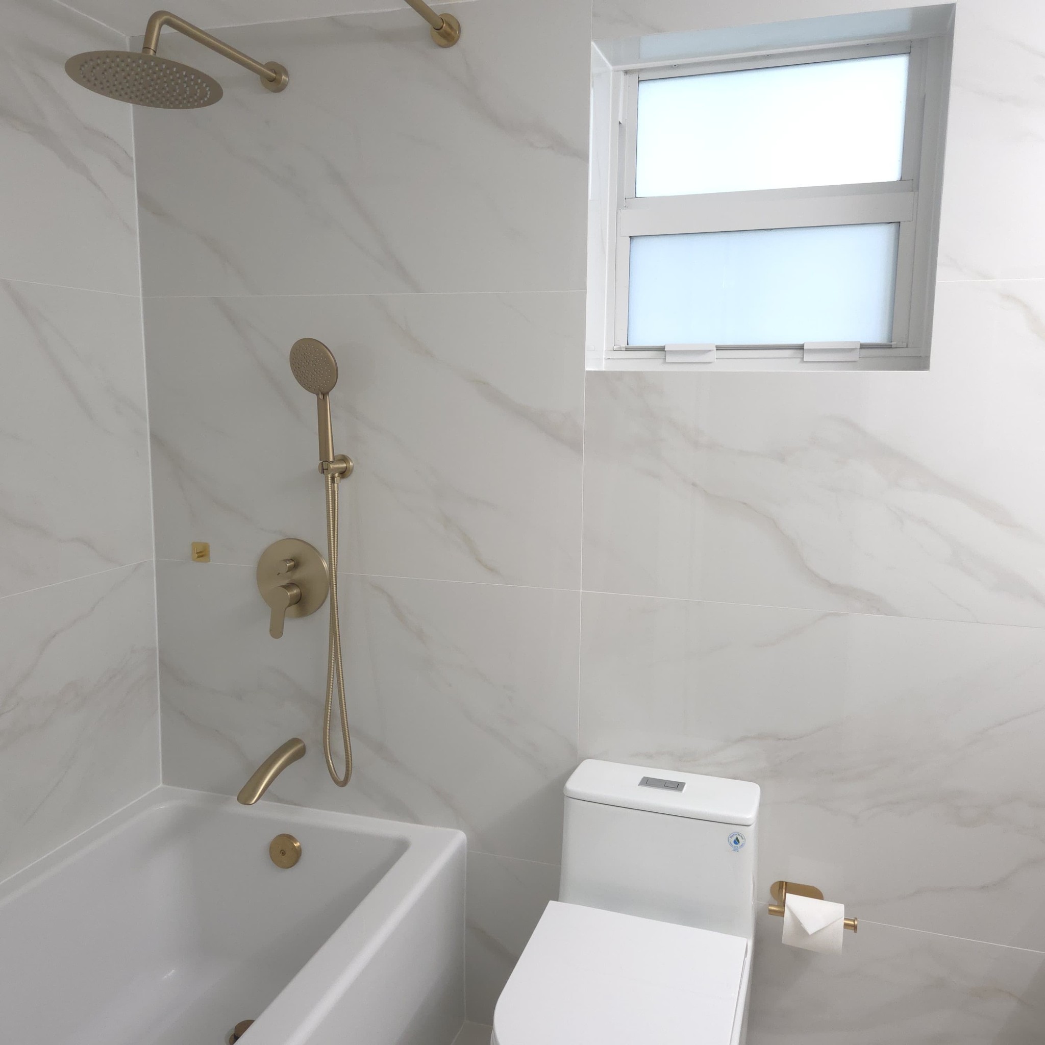 Original Real estate property photo: The photo showcases a bathroom with clean white tiling and modern fixtures under soft natural light. The image appears slightly underexposed, causing the details in the shadows to be less visible, and there is a slight cool tone present in the lighting. Enhancements will focus on improving the overall brightness, adjusting the contrast for clarity, and correcting the white balance to achieve a more natural, inviting look.
