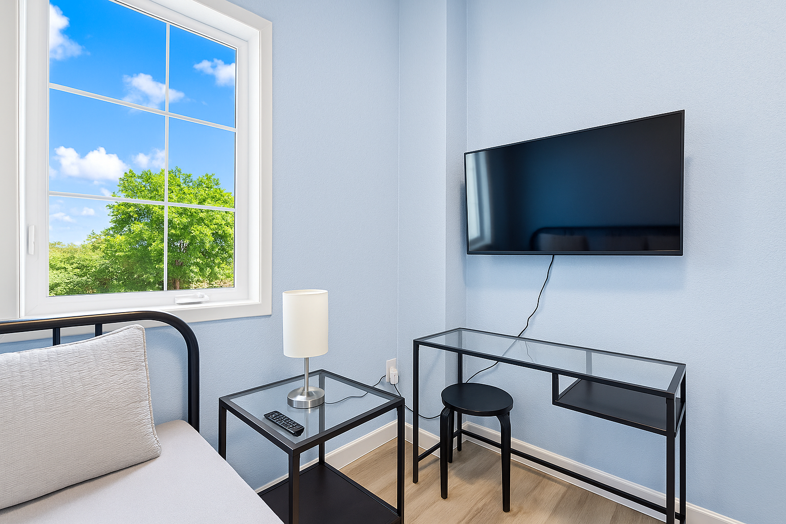 Enhanced Corner of a room with wall-mounted TV, glass table, and lamp against blue walls.