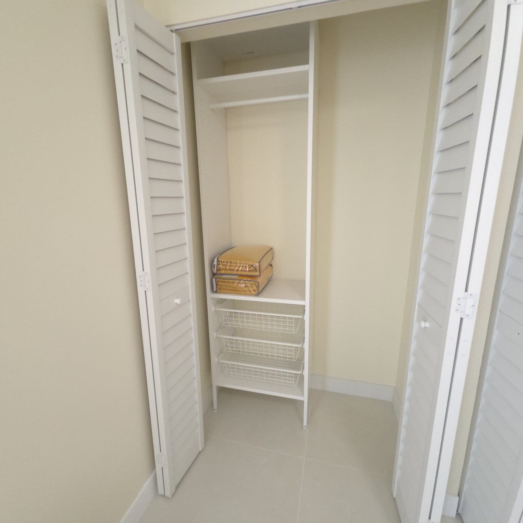 Original Real estate property photo: The photo shows a simple closet space with neutral tones, featuring light cabinetry and shelving. The image has slightly dull lighting and a warm color cast, likely due to the beige walls. To better showcase the closet's functionality, we will enhance the brightness and contrast, and correct the color balance for a more neutral and natural appearance, adhering to MLS standards.