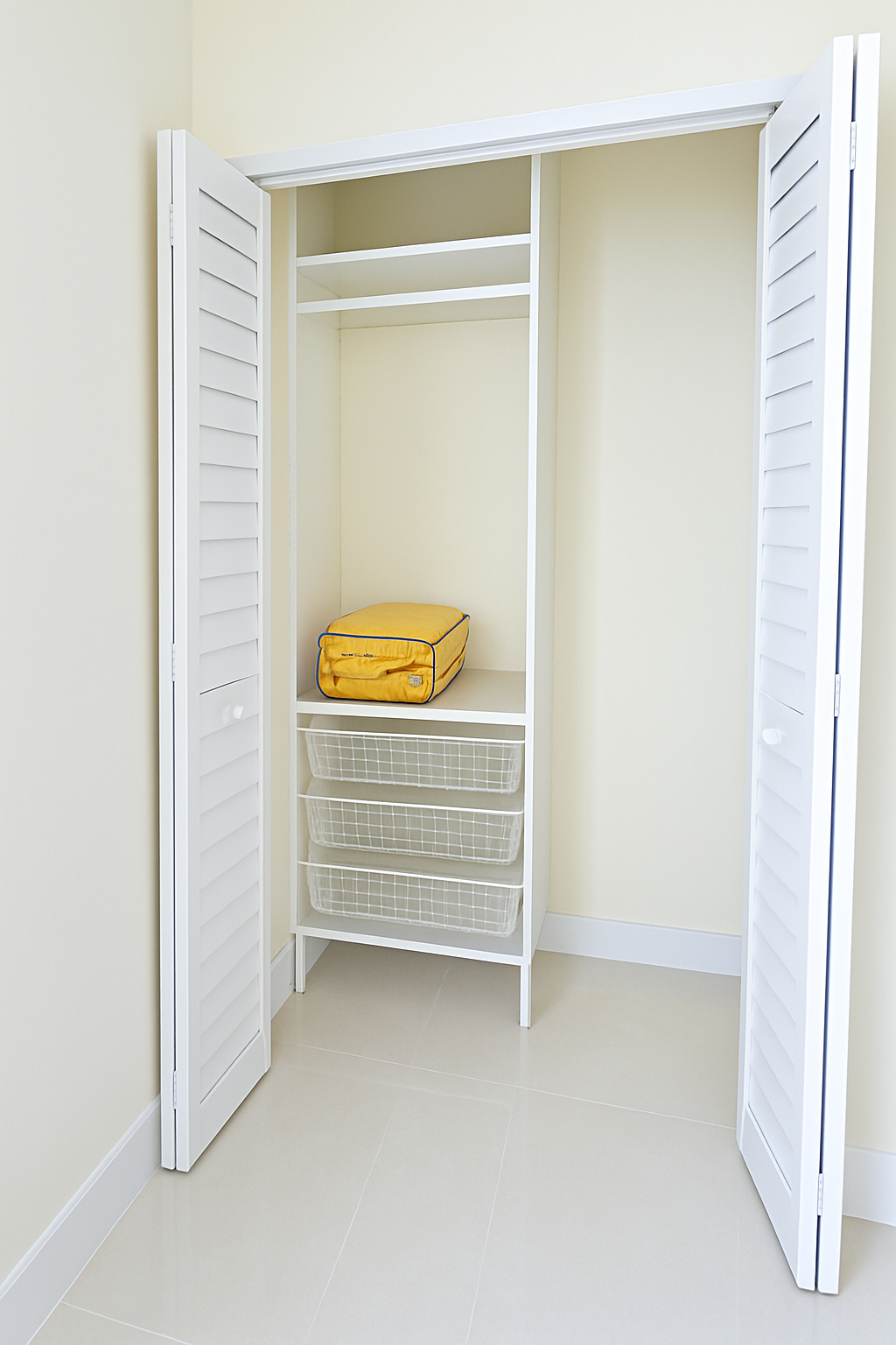 Enhanced Real estate property photo: The photo shows a simple closet space with neutral tones, featuring light cabinetry and shelving. The image has slightly dull lighting and a warm color cast, likely due to the beige walls. To better showcase the closet's functionality, we will enhance the brightness and contrast, and correct the color balance for a more neutral and natural appearance, adhering to MLS standards.