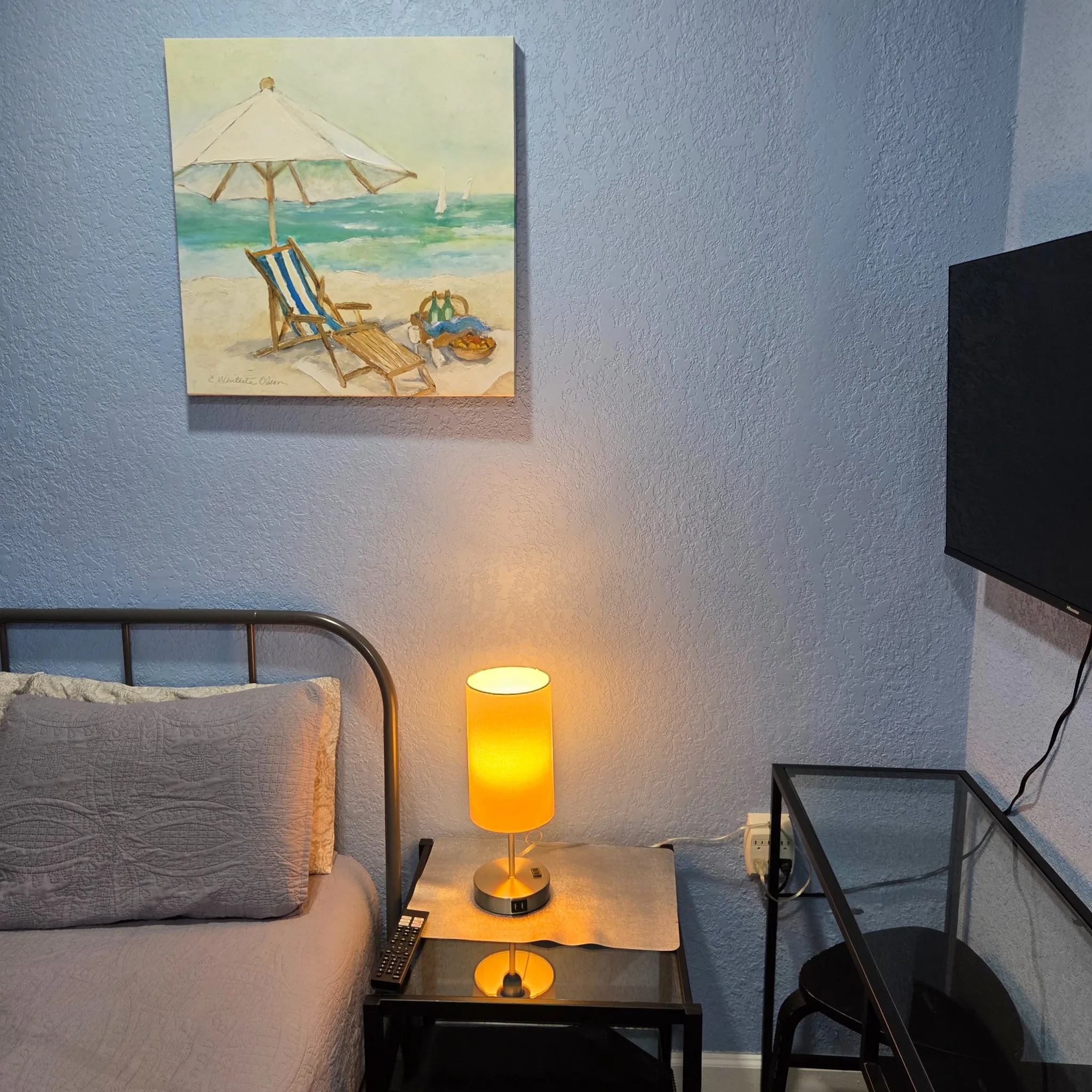 Original Bedroom corner with a bed, side table, a lamp, wall art, and a mounted TV against blue walls.