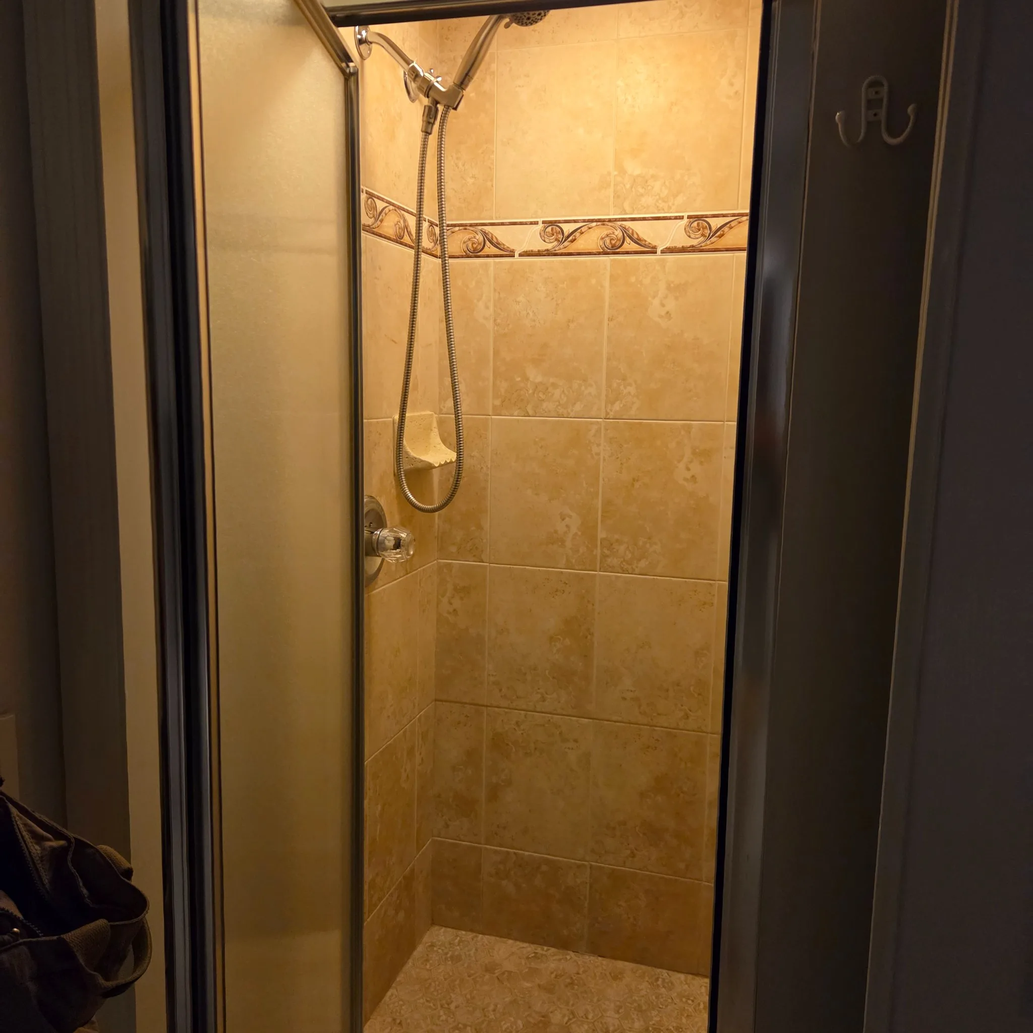 Original Shower with beige tiles and metal shower head, partially enclosed by a glass door.