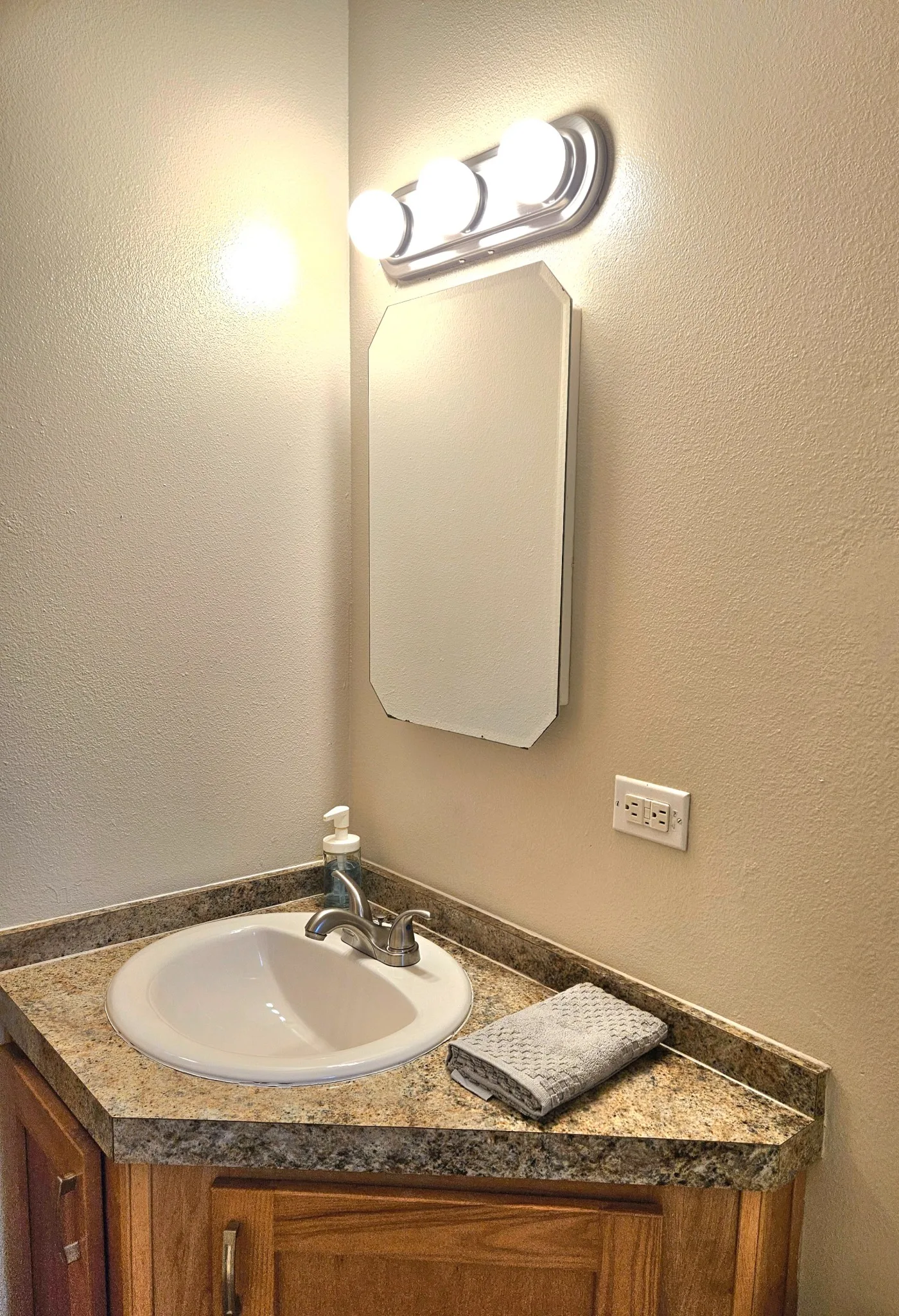Original Bathroom vanity with a granite countertop, mirror, and light fixture. Includes a sink, faucet, and towel.