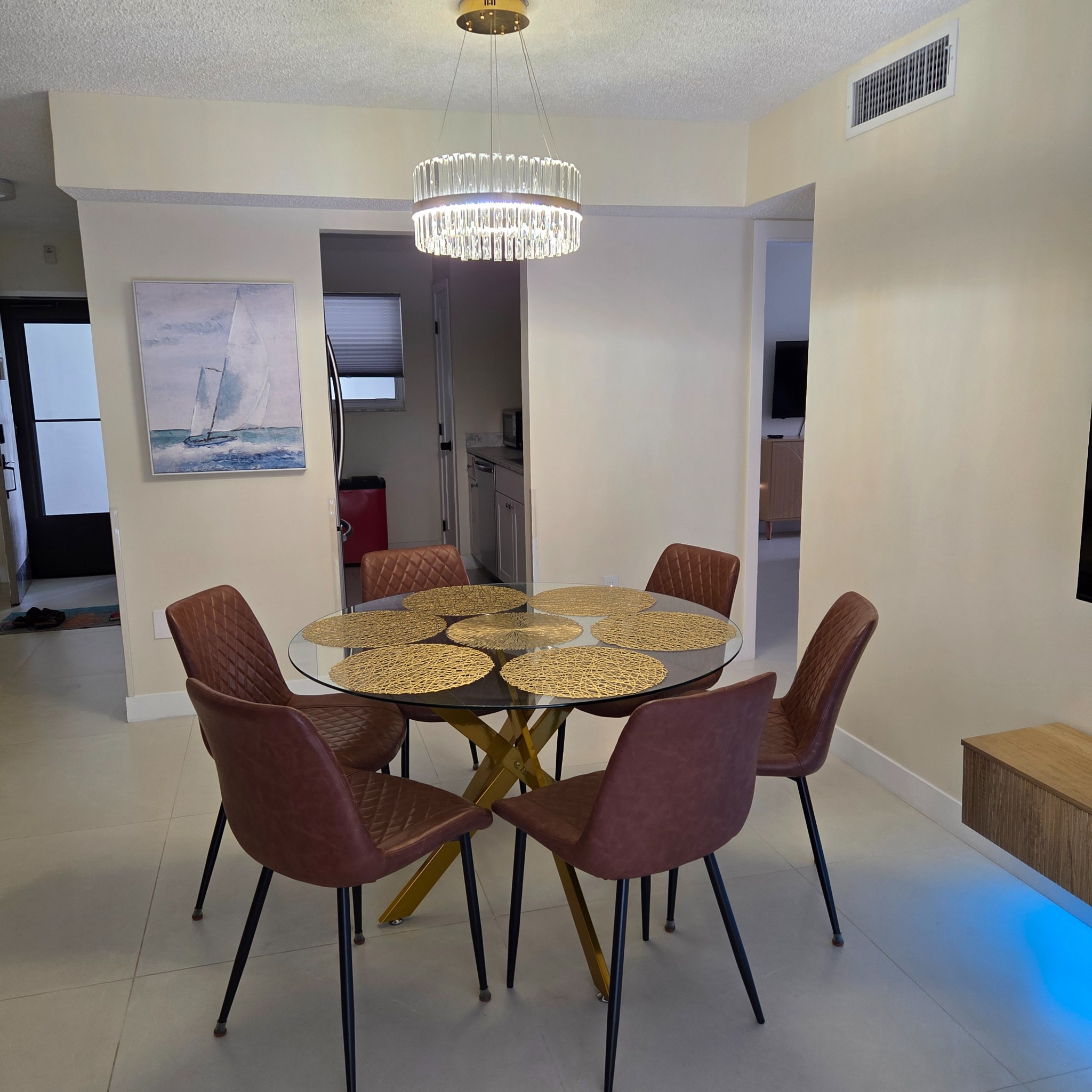 Original Real estate property photo: The photo shows a modern dining area with warm tones and good natural lighting. However, the image appears slightly dim, and the colors could be enhanced to better showcase the details of the furniture. The lighting could be balanced to ensure all areas are evenly illuminated, minimizing shadows.
