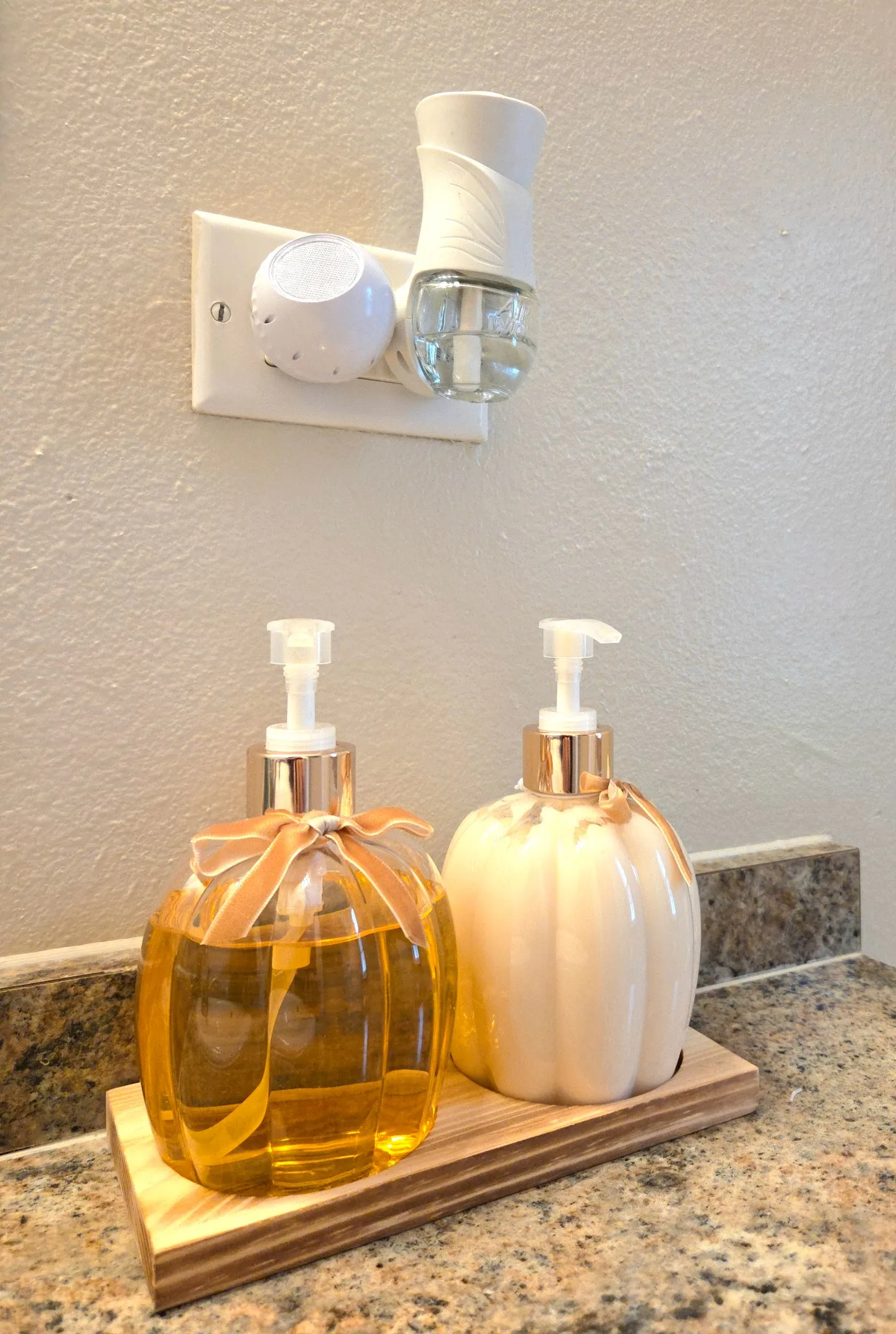Original Bathroom countertop with soap dispensers and air freshener, featuring a granite surface and wall outlet.