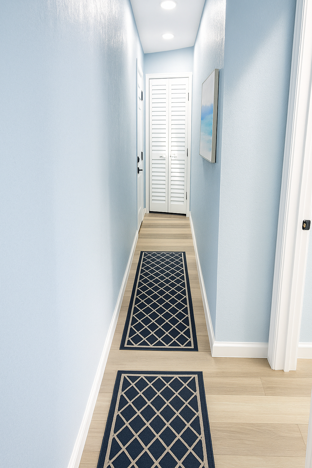Enhanced A narrow hallway with light gray walls, wooden flooring, and a decorative rug leading to a door with white shutters.