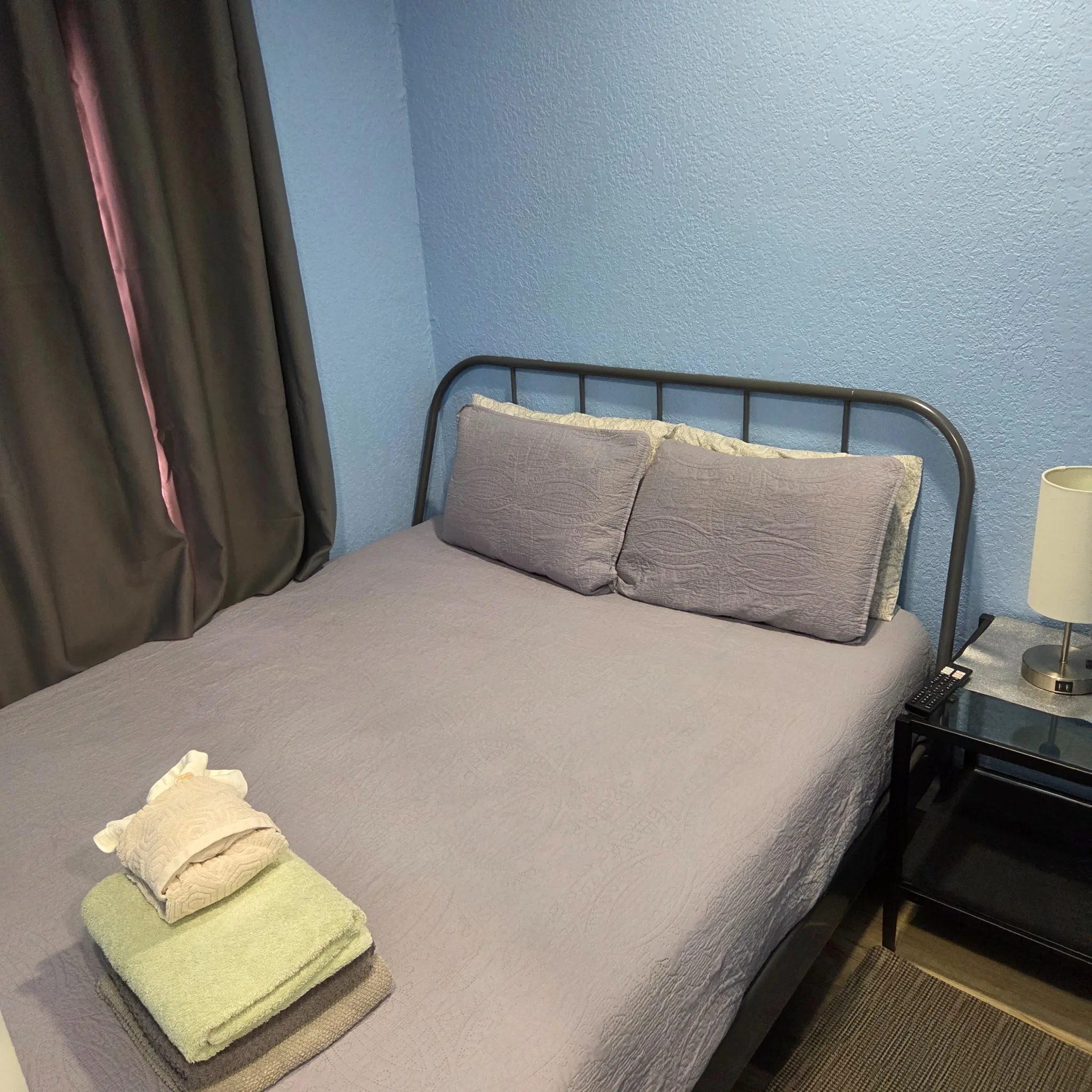 Original Bedroom with a metal-framed bed, blue walls, and a side table with a lamp.