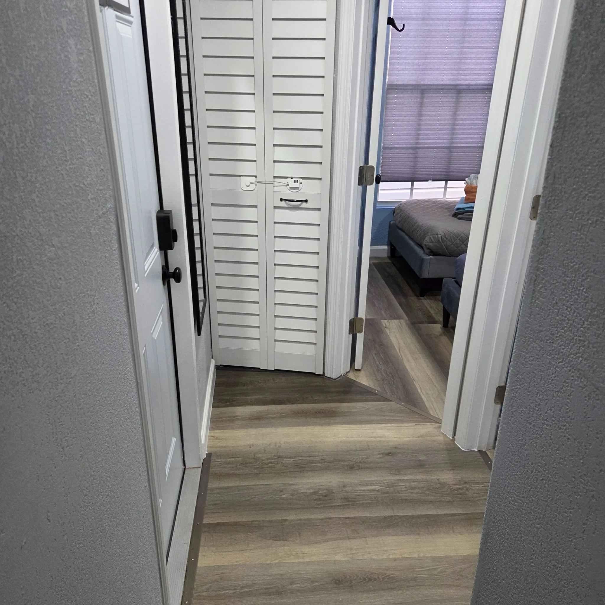 Original Hallway with wooden flooring, leading to a bedroom with a bed, showing white doors and a closet.