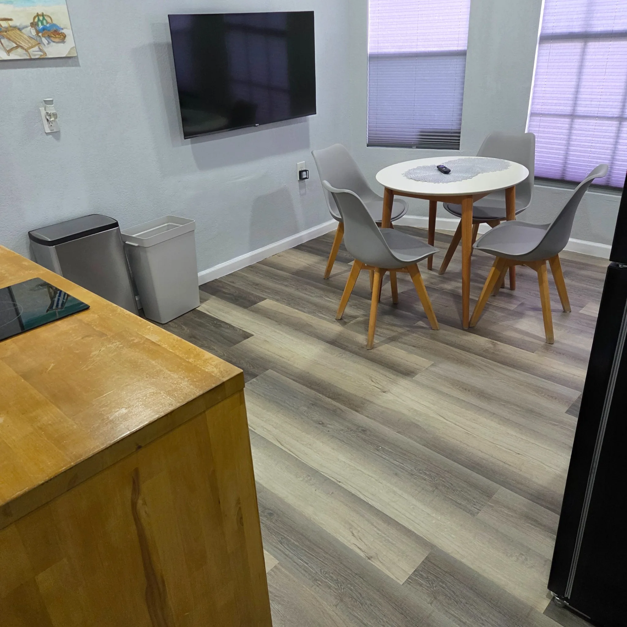 Original Dining area with four chairs, a round table, and a wall-mounted TV under natural lighting.